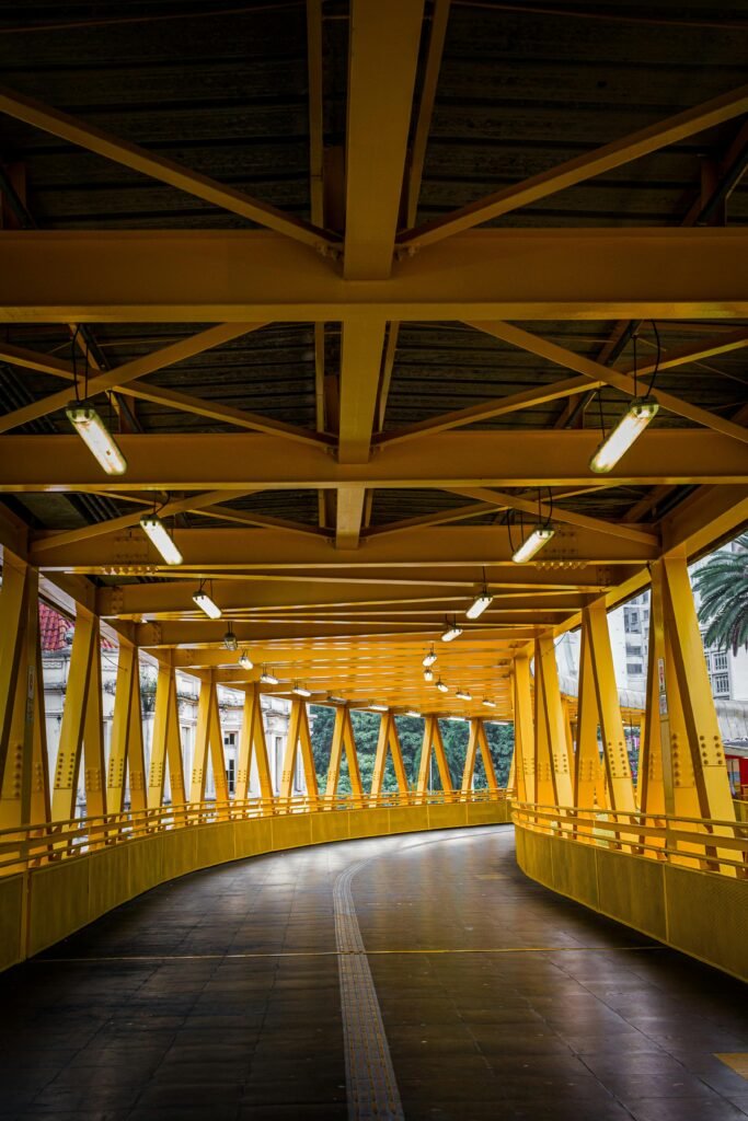 A curving yellow footbridge with modern geometric architecture and bright lighting.