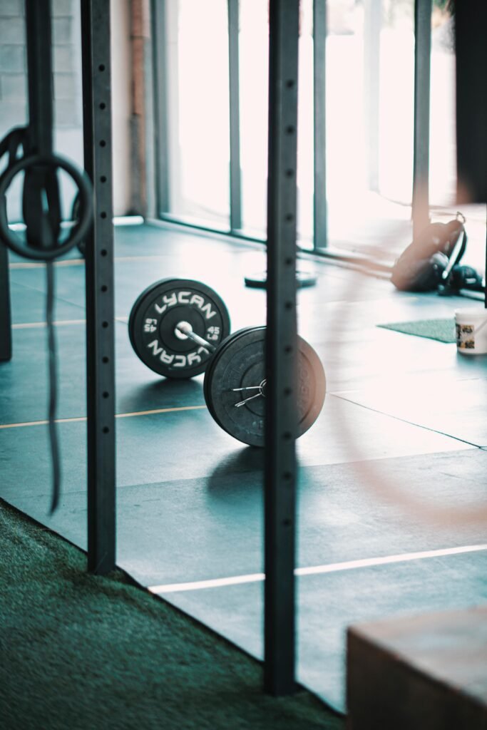 A solitary barbell rests on the gym floor, illuminated by natural light.